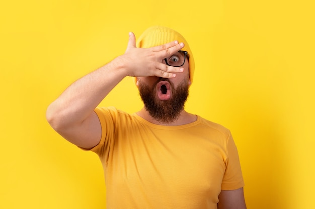 Hombre sorprendido mirando a través de los dedos sobre fondo amarillo