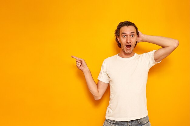 El hombre sorprendido señala con el dedo índice un espacio vacío para texto sobre un fondo amarillo