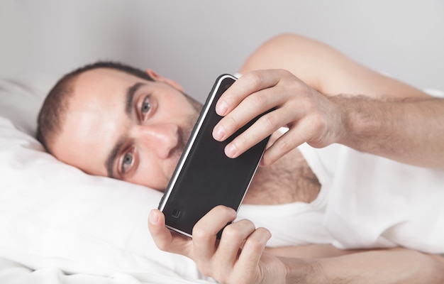 Hombre sorprendido con smartphone en la cama.