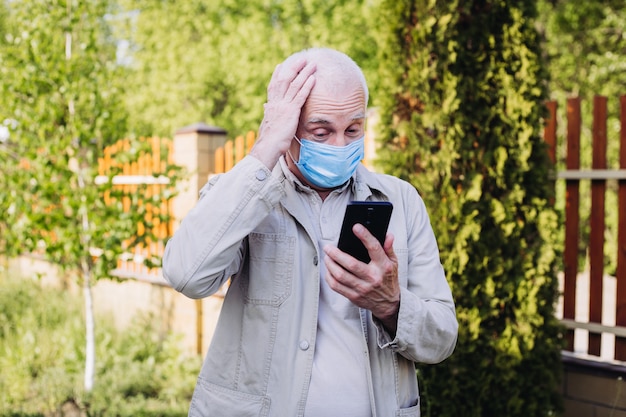 Hombre sorprendido y sorprendido con una mascarilla médica que usa el teléfono para buscar noticias