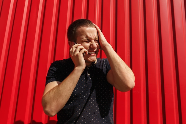 Foto hombre sorprendido usando su teléfono celular en la pared roja