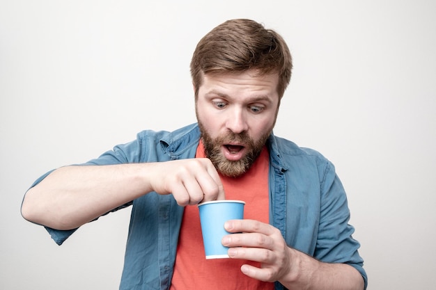 Hombre sorprendido con un vaso de papel en la mano saca algo del té recién bebido con sorpresa