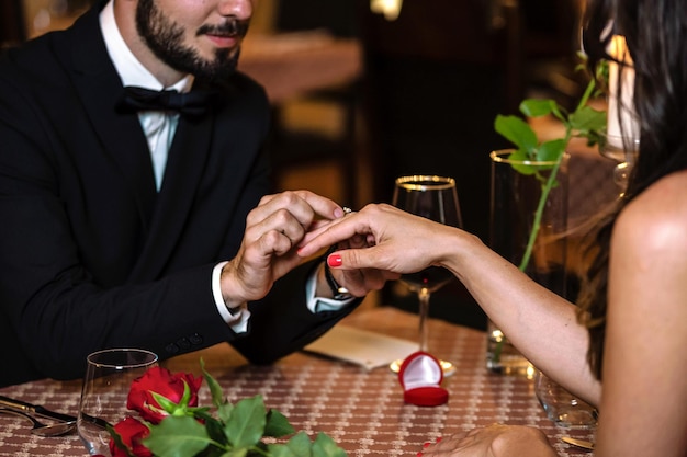 Hombre sorprendiendo a mujer con anillo de compromiso durante una cena romántica en el restaurante en primer plano