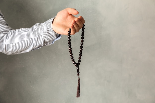 Foto hombre sostenga cuentas de oración en la mano contra el fondo gris