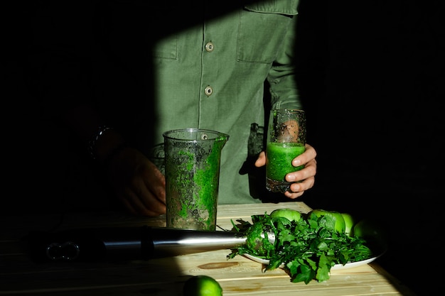 Foto hombre sostenga en la mano vidrio con batido de desintoxicación saludable, cocinar con licuadora con frutas frescas y espinacas verdes, concepto de desintoxicación de estilo de vida. concepto de desintoxicación de estilo de vida. bebidas veganas.