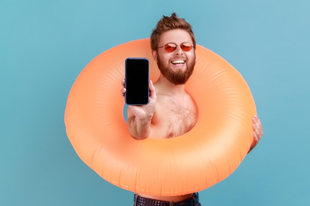 Hombre sosteniendo un anillo de goma naranja y mostrando un teléfono con pantalla en blanco para publicidad