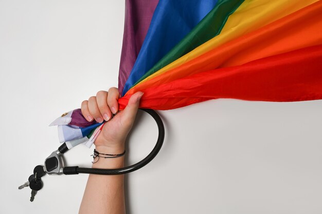 Hombre sosteniendo la bandera del arco iris de textura de tela para LGBT con cadena de metal y candado sobre fondo blanco. Concepto de amor y libertad.