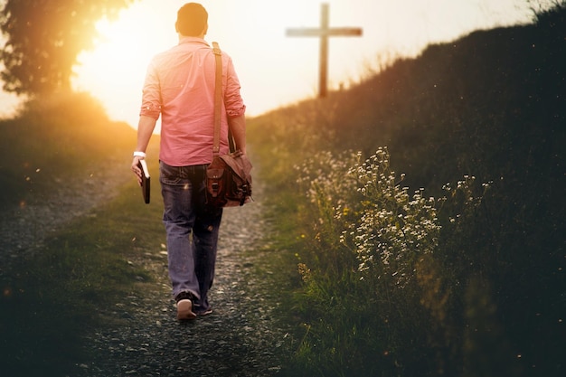 Hombre sosteniendo la biblia caminando hacia la colina hacia la cruz con un fondo borroso