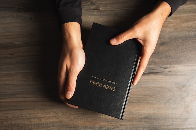 Un hombre sosteniendo una Biblia en la mesa. vista desde arriba