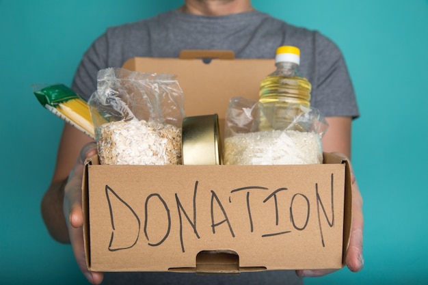 Un hombre sosteniendo una caja de donación de diferentes productos.