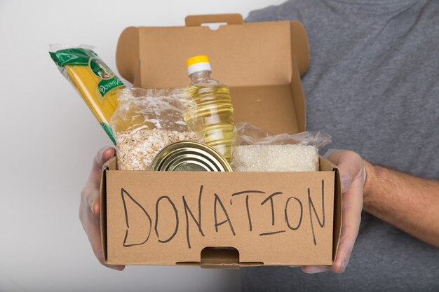 Un hombre sosteniendo una caja de donación de diferentes productos.