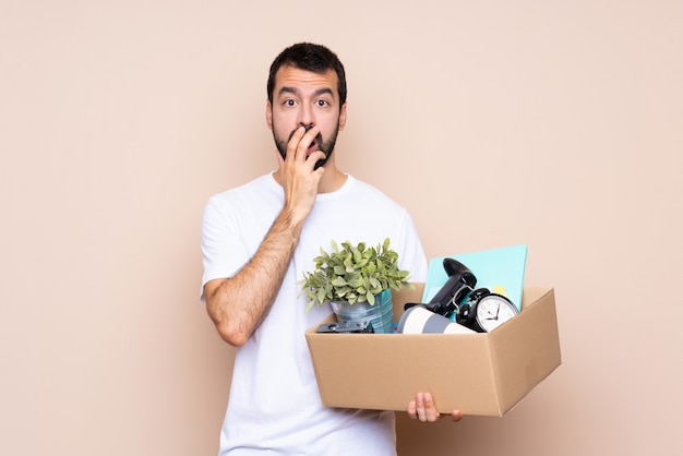 Hombre sosteniendo una caja y mudarse a una nueva casa sorprendido y conmocionado mientras mira a la derecha