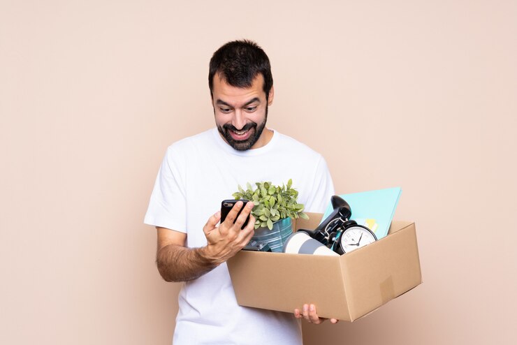 Foto hombre sosteniendo una caja y mudarse a una nueva casa sorprendido y enviando un mensaje