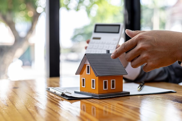 Hombre sosteniendo una calculadora y apuntando un modelo de una casa sobre una mesa, un vendedor mostrando números calculando el costo de reservar un proyecto de vivienda en el proyecto. Concepto de comercio de bienes raíces.