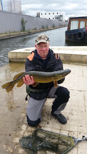 Foto hombre sosteniendo la captura de pescado en el muelle