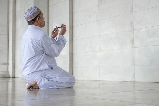 Hombre sosteniendo cuentas de oración mientras reza en la mezquita