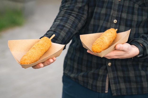 Hombre sosteniendo dogi de maíz en platos de papel sobre fondo borroso comida callejera coreana