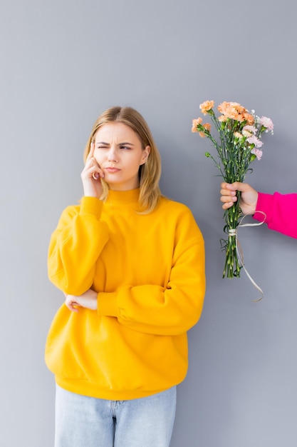 hombre sosteniendo flores para una mujer con ropa amarilla en un fondo gris Feliz día