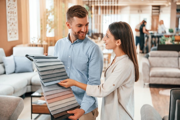 Hombre sosteniendo materiales de diferentes colores para elegir Pareja buscando el sofá y la cama en la tienda