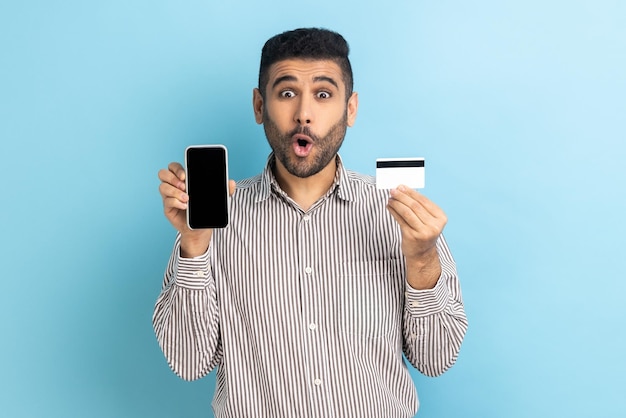 Hombre sosteniendo y mostrando un teléfono inteligente con pantalla vacía y una tarjeta de crédito sorprendido con la banca móvil fácil