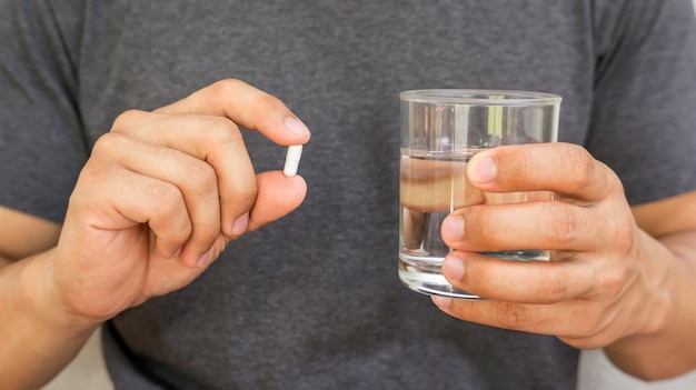 Hombre sosteniendo una pastilla y un vaso de agua.