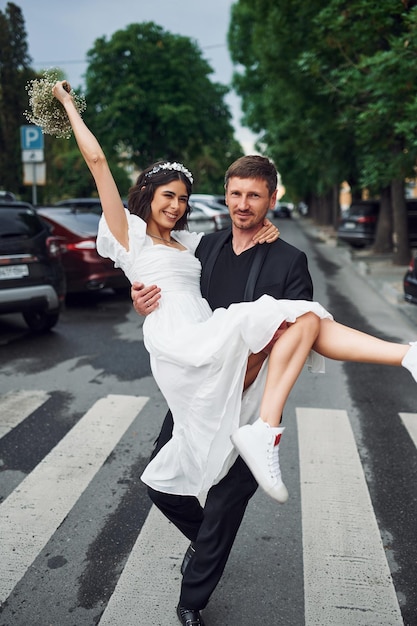 Hombre sosteniendo a su mujer en las manos Hermosa novia con su prometido está celebrando la boda al aire libre