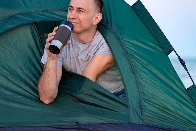 Hombre sosteniendo una taza de café en la carpa por la mañana disfrutando del ocio Concepto de viajar senderismo acampar