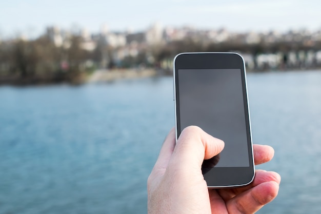 hombre sosteniendo un teléfono celular con el río en el fondo