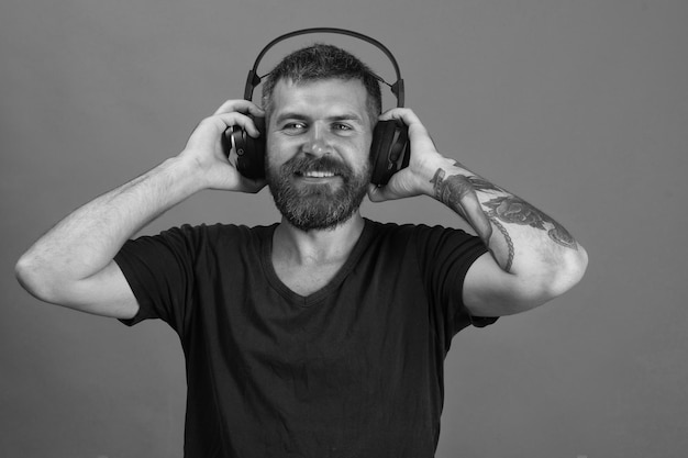 Hombre sostiene auriculares sobre fondo azul Dj con barba