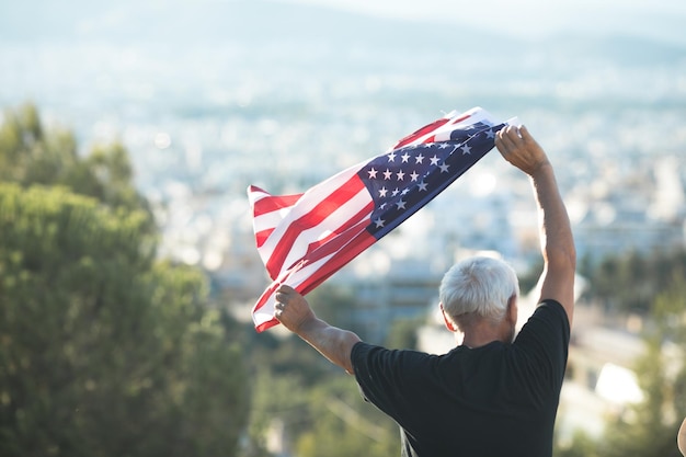 Un hombre sostiene una bandera estadounidense frente a un paisaje urbano.