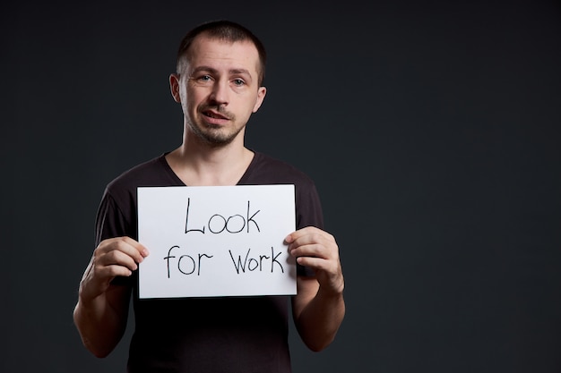 El hombre sostiene un cartel con las palabras en busca de trabajo, desempleo y crisis.