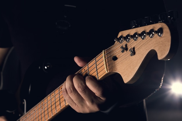 Un hombre sostiene una guitarra eléctrica en un fondo negro, un enfoque selectivo en la mano.