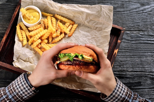 El hombre sostiene la hamburguesa en las manos. Comida con hamburguesa y papas fritas.