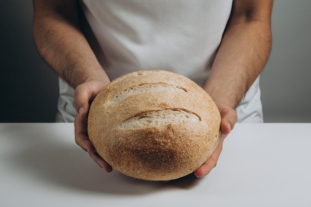 Un hombre sostiene una hogaza redonda de pan de masa fermentada en sus manos