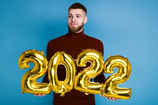 Un hombre sostiene los números 2022 de globos dorados. El próximo año nuevo