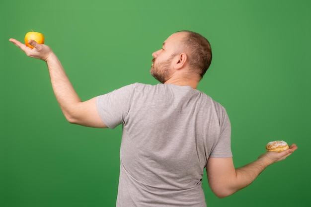 Un hombre sostiene un pastel y una manzana sobre un fondo verde La elección entre alimentos saludables y no saludables Estilo de vida saludable u obesidad