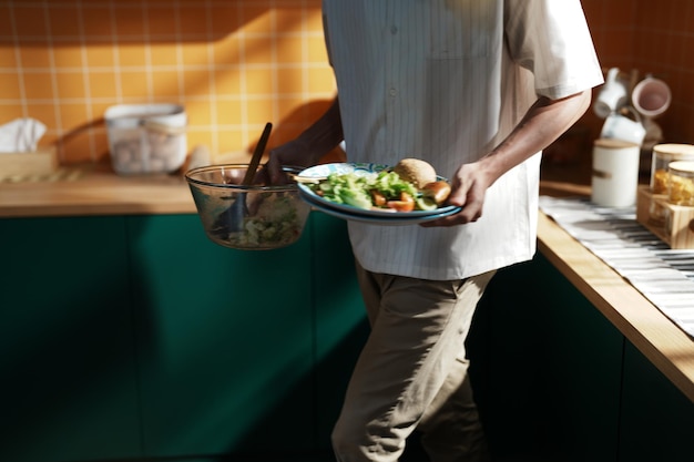 Un hombre sostiene un plato de comida frente a una pared verde.