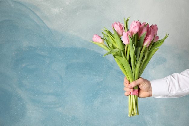 El hombre sostiene el ramo de tulipanes rosados en azul, espacio para texto