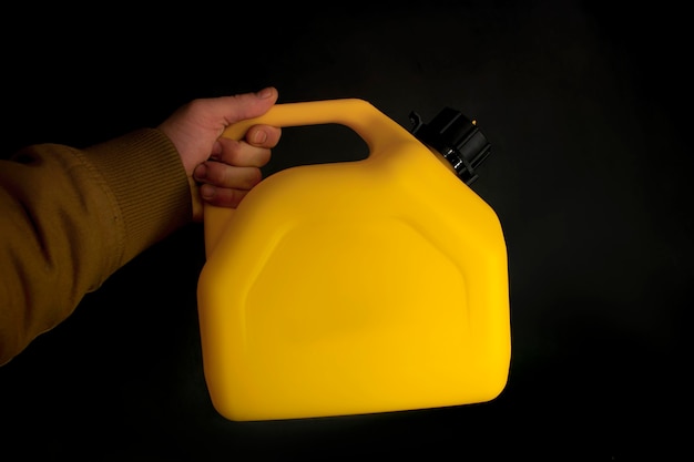 El hombre sostiene un recipiente de plástico amarillo para combustible de automóvil en su mano sobre un fondo negro. Maqueta de un contenedor para líquidos y combustibles peligrosos.