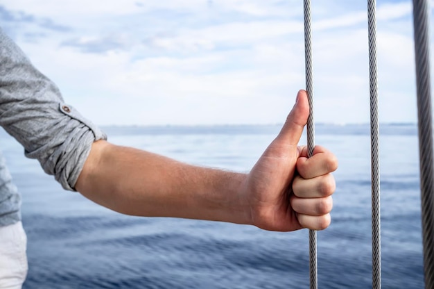 Foto el hombre sostiene su mano con el pulgar hacia arriba sobre el tipo de metal en el yate.