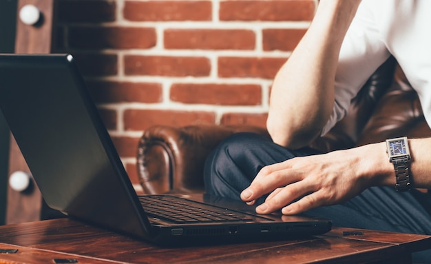 Un hombre sostiene su mano en el touchpad del portátil. Se sienta en un sillón marrón en su propio armario.