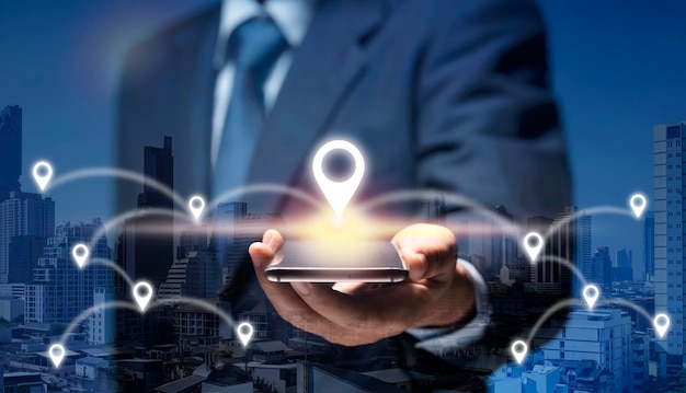 El hombre sostiene el teléfono inteligente y se conecta al icono de ubicación GPS que muestra el negocio global, la dirección, los viajes, el concepto 5G. El hombre de negocios utiliza la red de Internet en el teléfono móvil y encuentra la ubicación en la ciudad mediante el mapa del navegador GPS.
