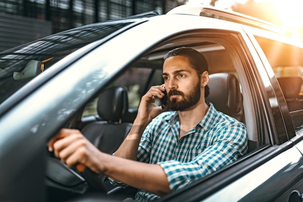 El hombre sostiene un teléfono inteligente en la mano y habla mientras conduce un automóvil.