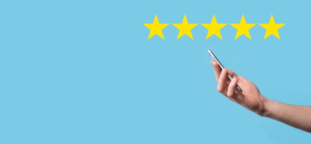 El hombre sostiene el teléfono inteligente en las manos y da una calificación positiva, icono símbolo de cinco estrellas para aumentar la calificación del concepto de empresa en la superficie azul