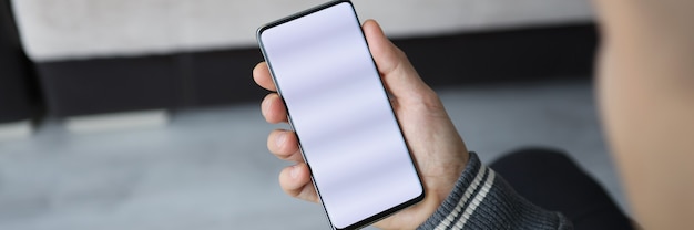 El hombre sostiene el teléfono inteligente con pantalla en blanco en la mano
