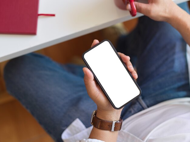 El hombre sostiene el teléfono inteligente con pantalla simulada en la mano mientras se ubica en el lugar de trabajo