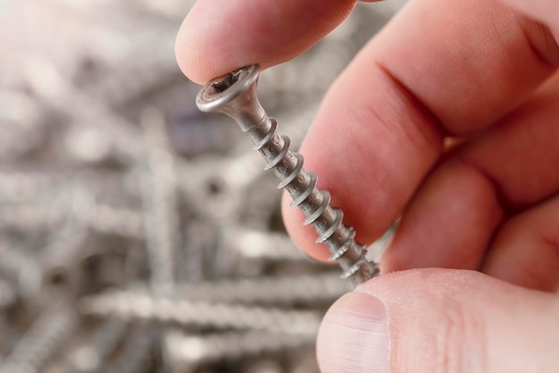 Un hombre sostiene un tornillo tornillos de primer plano para la producción de herramientas de reparación y reparación de muebles de madera st...