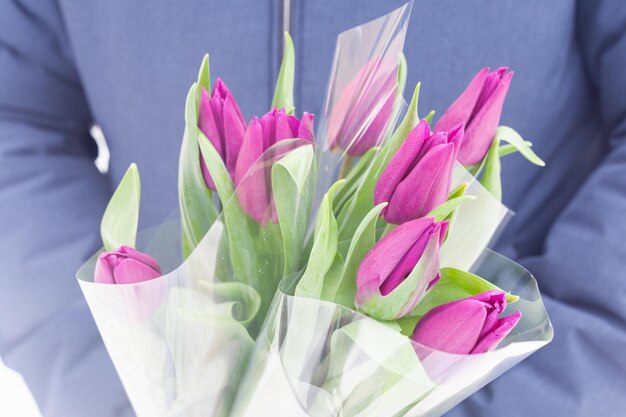 Un hombre sostiene varios ramos de tulipanes morados en sus manos. Un regalo para una celebración festiva, un estado de ánimo primaveral. Sorpresa romantica