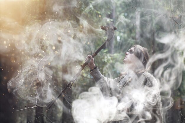 Un hombre con una sotana pasa un ritual en un bosque oscuro con una bola de cristal y un libro.