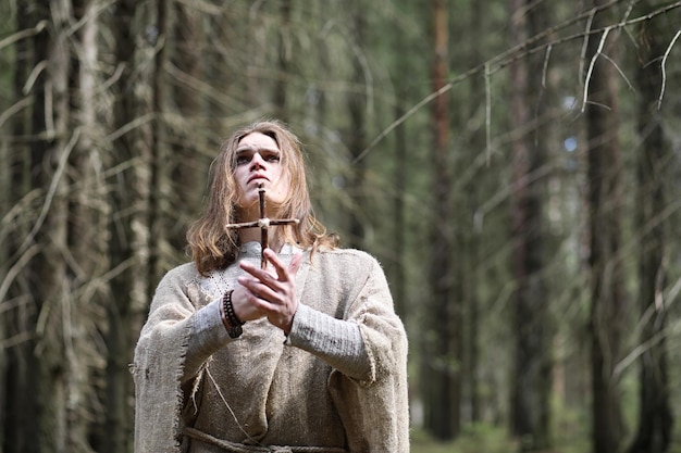 Un hombre con una sotana pasa un ritual en un bosque oscuro con una bola de cristal y un libro.